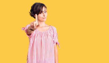 Kısa saçlı, günlük giysiler giyen güzel genç bir kadın parmağını kaldırmış ve kızgın bir ifadeyle işaret ediyor. 