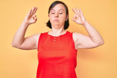 Down sendromlu esmer kadın günlük kıyafetler giyiyor rahatla ve gözleri kapalı gülümse parmaklarıyla meditasyon hareketi yapıyor. yoga konsepti. 
