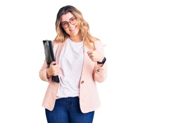 İş kıyafetleri ve gözlük takan genç beyaz kadın elinde güler yüzlü, mutlu ve olumlu bir şekilde gülümseyen, başparmağıyla mükemmel ve onay işareti yapan. 