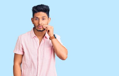 Yazlık tişört giyen yakışıklı Latin Amerikalı genç adam. Ağzı ve dudakları parmaklarıyla kapalı. gizli ve sessiz, tabu konuşması 