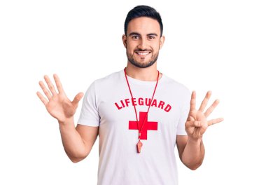 Cankurtaran üniforması giyen yakışıklı genç adam dokuz numarayı gösterip işaret ederken kendinden emin ve mutlu gülümsüyor.. 