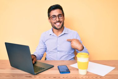 Ofiste çalışan genç İspanyol bir adam bir fincan kahve içip mutlu ve gururlu birini işaret ediyor. 