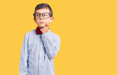 Sevimli sarışın çocuk inek papyonu takıyor ve gözlük takıyor. Ciddi bir yüz ifadesi var. Soru sormayı düşünüyor. 