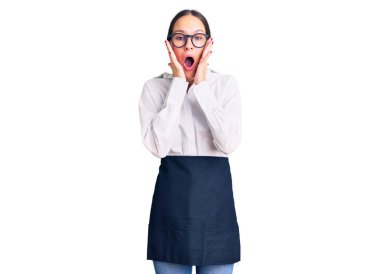 Güzel, esmer, profesyonel garson önlüğü giymiş genç bir kadın. Korkmuş ve şok olmuş. Şaşırmış ve hayrete düşmüş. 