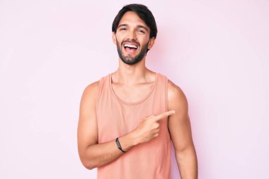 Yakışıklı İspanyol bir adam, günlük kıyafetler giyiyor, neşeli, yüzünde mutlu ve doğal bir ifadeyle, elleri ve parmaklarıyla yüzünü gösteren bir gülümseme var. 