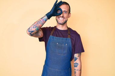 Dövmeli, berber önlüklü, gülümseyen yakışıklı genç adam mutlu görünüyor. 