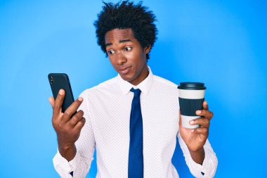 Afro saçlı, akıllı telefon kullanan, bir fincan kahve içen, gülümseyen ve kafasını çeviren yakışıklı Afro-Amerikan erkeği.. 