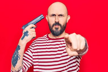 Genç ve yakışıklı bir adam elinde silahla kameraya ve sana bakıyor. Kendine güvenen bir jest, ciddi görünüyor. 