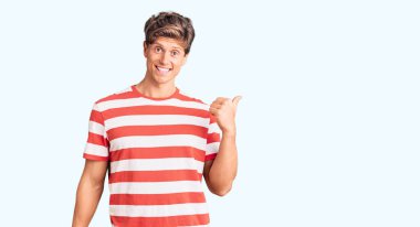 Genç, yakışıklı, sıradan kıyafetler giyen, gülen yüzlü, gülümseyen ve baş parmağıyla yan tarafı gösteren bir adam.. 