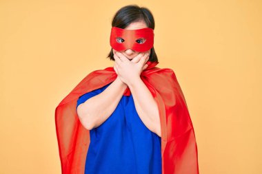 Down sendromlu esmer kadın süper kahraman kostümü giyiyor. Ağzını yanlışlıkla ellerle kapatıyor. gizli kavram. 