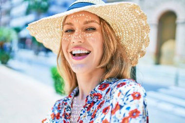 Yaz şapkası takmış, mutlu bir şekilde gülümseyen güzel sarışın bir kadın. Şehrin caddesinde yüzünde gülümsemeyle dikilirken.