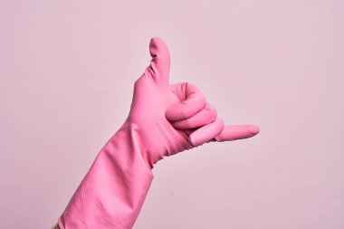 İzole edilmiş pembe arka plan üzerinde temizlik eldiveni ile beyaz bir gencin eli Hawaii Shaka selamlama hareketi, telefon ve iletişim sembolü.