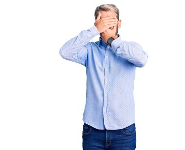 Zarif gömlek giyen yakışıklı sarışın genç adam gözlerini ve ağzını elleriyle kapatıyor, şaşırmış ve şok olmuş. duygu gizleme 