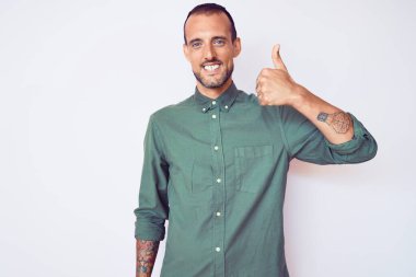 Dövmeli genç, sıradan kıyafetler giyen mutlu ve pozitif gülümseyen, başparmağı mükemmel ve onay işareti yapan yakışıklı bir adam. 