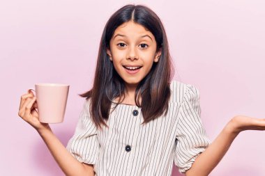 Güzel kız elinde kahveyle başarıyı kutluyor. Mutlu bir gülümseme ve kaldırılmış bir el ile kazanan bir ifade. 