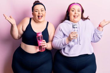 Genç ve cüsseli ikizler spor kıyafetleri giyip bir şişe su içerek zaferi mutlu bir gülümsemeyle ve kazanan yüz ifadesini kaldırarak kutluyorlar. 