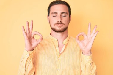 Gündelik kıyafetler giyen genç yakışıklı adam rahatla ve gözleri kapalı gülümse parmaklarıyla meditasyon hareketi yapıyor. yoga konsepti. 