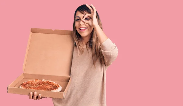 年轻而漂亮的女人拿着装有披萨的纸盒 高兴地微笑着 手拿着手签 用手指看过去 — 图库照片