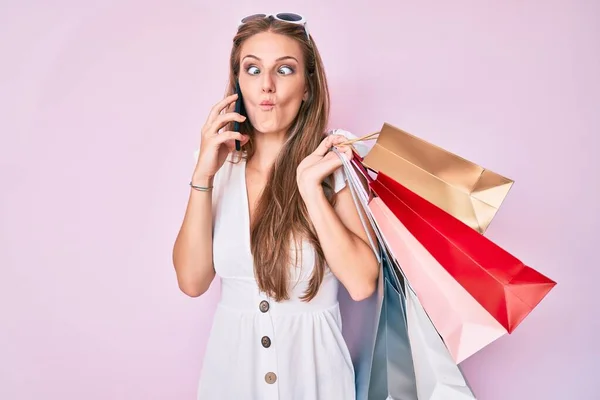 Jovem Loira Segurando Sacos Compras Falando Smartphone Fazendo Cara Peixe — Fotografia de Stock