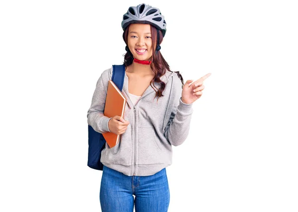 若いです美しいです中国の女の子身に着けている学生のバックパックと自転車ヘルメット保持本笑顔幸せなポインティングとともに手と指へ側 — ストック写真