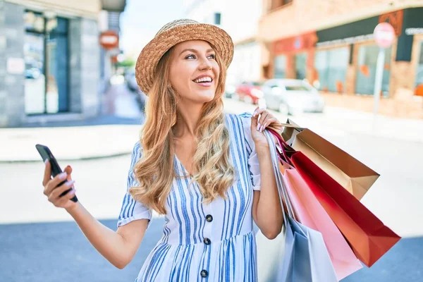 아름다운 점원이 웃으며 쇼핑백을 가게에 행복하게 갑니다 스마트폰을 사용하여 행복하게 — 스톡 사진