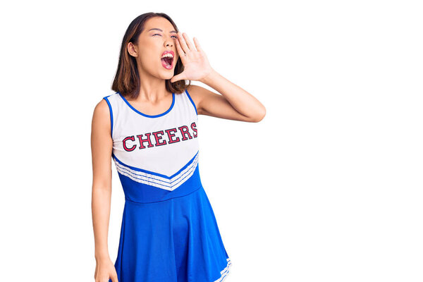 Young beautiful chinese girl wearing cheerleader uniform shouting and screaming loud to side with hand on mouth. communication concept. 
