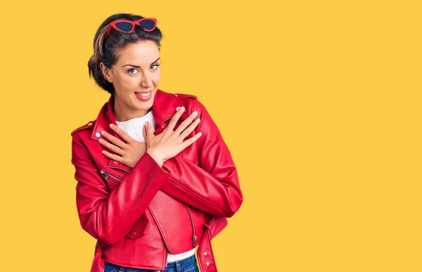 Young beautiful woman wearing red leather jacket smiling with hands on chest with closed eyes and grateful gesture on face. health concept.