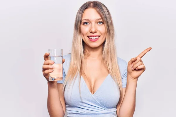 Young Beautiful Blonde Girl Drinking Glass Water Smiling Happy Pointing — ストック写真