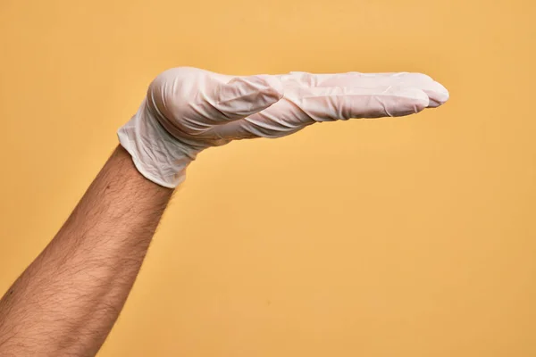 Mão Homem Jovem Caucasiano Com Luva Médica Sobre Fundo Amarelo — Fotografia de Stock