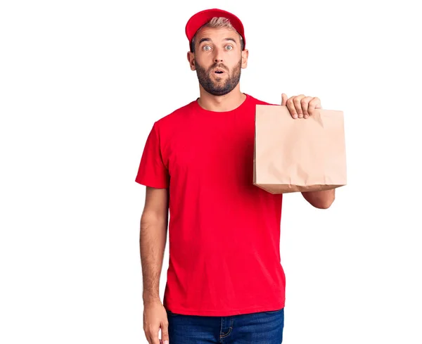 Young Handsome Blond Man Holding Delivery Paper Bag Scared Amazed — Stock Photo, Image