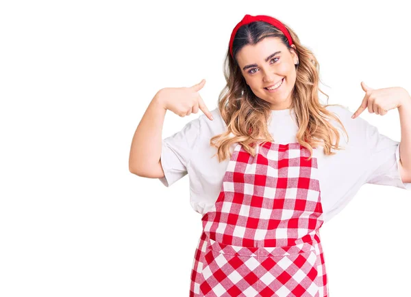 Young caucasian woman wearing apron looking confident with smile on face, pointing oneself with fingers proud and happy.