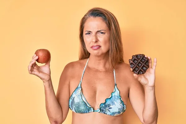 Mulher Hispânica Meia Idade Segurando Maçã Donut Expressão Indolor Confuso — Fotografia de Stock