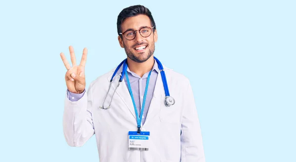 身穿医生制服 头戴听诊器的年轻人 带着自信和快乐的笑容 用第三指尖示人 — 图库照片