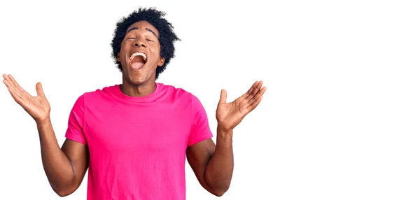 アフロの髪をしたハンサムなアフリカ系アメリカ人男性は 腕を上げて興奮して叫んで目を閉じて成功のために狂気と狂気を祝うカジュアルなピンクのTシャツを着ています 勝者のコンセプト — ストック写真