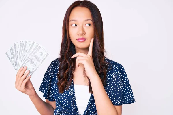 Jovem Menina Chinesa Bonita Segurando Dólares Rosto Sério Pensando Sobre — Fotografia de Stock