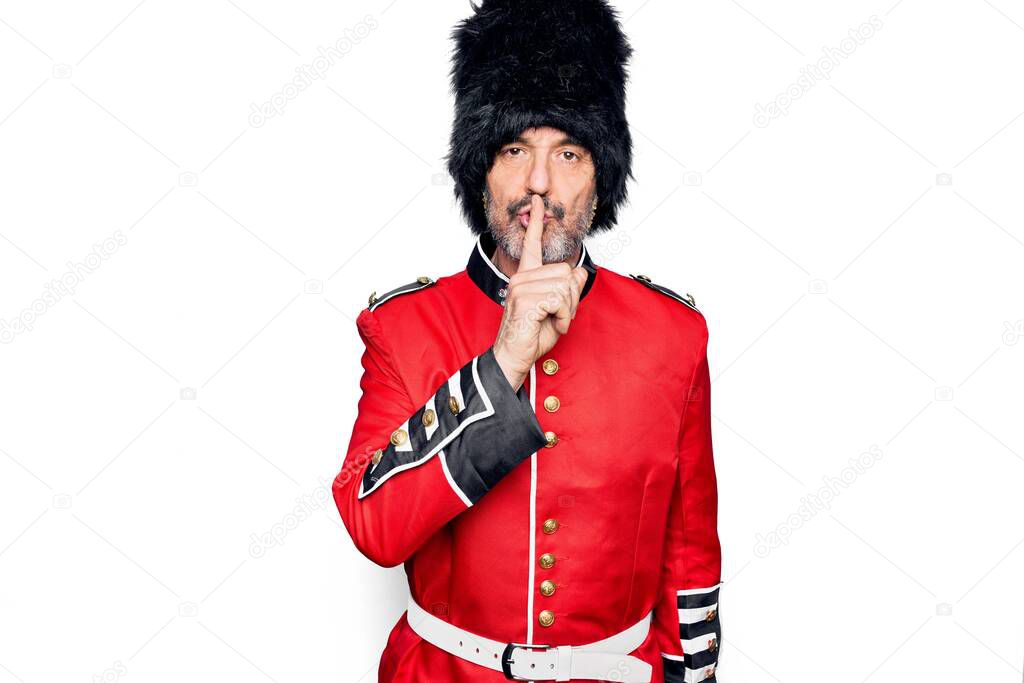 Middle age handsome wales guard man wearing traditional uniform over white background asking to be quiet with finger on lips. Silence and secret concept.