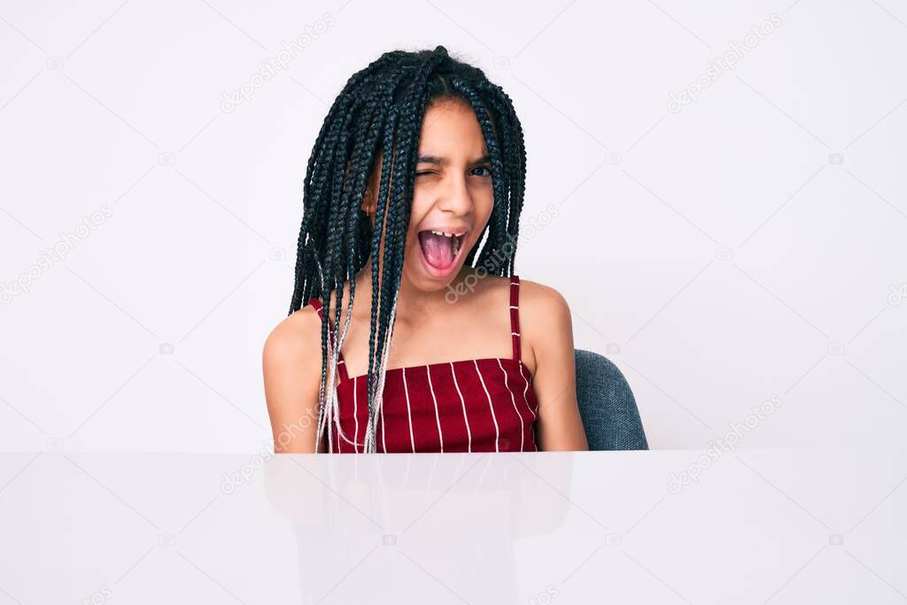 Young african american girl child with braids wearing casual clothes sitting on the table winking looking at the camera with sexy expression, cheerful and happy face. 