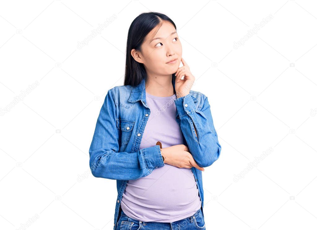 Young beautiful chinese woman pregnant expecting baby with hand on chin thinking about question, pensive expression. smiling and thoughtful face. doubt concept. 