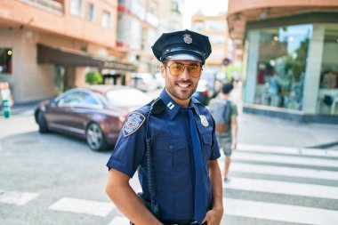 Polis üniforması giyen genç, yakışıklı İspanyol polis mutlu bir şekilde gülümsüyor..