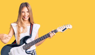 Güzel, beyaz, sarı saçlı, elektro gitar çalan, mutlu, eli ve parmağı olan bir kadın. 
