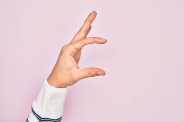 İzole edilmiş pembe arka plan üzerinde parmaklarını gösteren beyaz bir adamın eli. Görünmez bir şeyi alıp, parmaklarıyla uzayı gösteren bir nesneyi tutuyor.