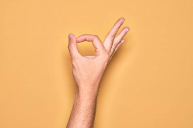İzole edilmiş sarı arka plan üzerinde parmaklarını gösteren beyaz bir gencin eli işaret ediyor. Onaylama ifadesi parmaklarıyla iyi bir sembol oluşturuyor.