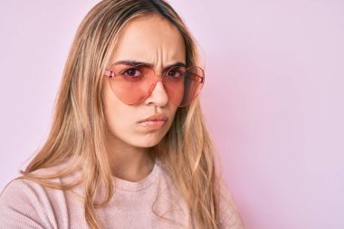 Kalp şeklinde güneş gözlüğü takan genç, sarışın kadın şüpheci ve gergin, sorun yüzünden surat asıyor. negatif kişi. 