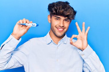 Genç İspanyol adam termometreyi tutuyor. Parmaklarıyla imza atıyor. Gülümsüyor. 