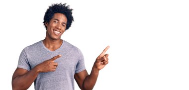 Yakışıklı Afro saçlı, sıradan giyinmiş, gülümseyen ve kameraya bakan iki eli ve parmakları yanda olan Afro-Amerikan bir adam.. 