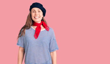 Fransız beresi ve çizgili tişört giyen, yüzünde mutlu ve havalı bir gülümseme olan genç ve güzel bir sarışın kadın. şanslı kişi. 