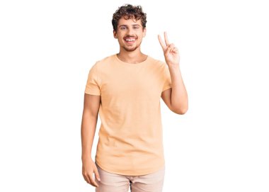 Kıvırcık saçlı, sıradan kıyafetler giyen, kameraya gülümseyen ve zafer işareti yapan genç yakışıklı bir adam. İki numara.. 