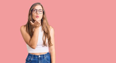 Güzel, beyaz tenli, sıradan kıyafetler ve gözlük takan bir kadın kameraya bakıp havada öpücükler savuruyor. Güzel ve seksi. aşk ifadesi. 