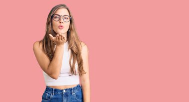 Beautiful caucasian young woman wearing casual clothes and glasses looking at the camera blowing a kiss with hand on air being lovely and sexy. love expression.  clipart