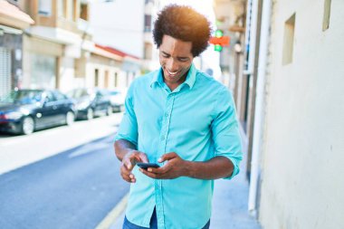 Genç, yakışıklı, Afro-Amerikan bir adam günlük giysiler giyip mutlu gülümsüyor. Yüzünde gülümsemeyle şehrin caddesinde akıllı telefon kullanarak dikiliyorsun..